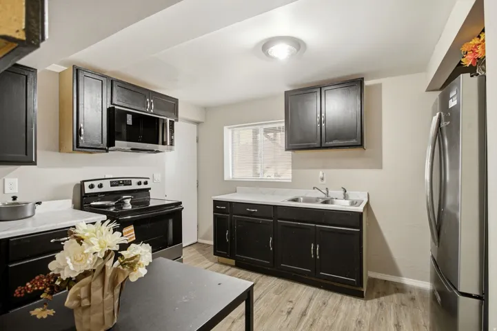 Kitchen featuring dark cabinetry, stainless steel appliances, wood-finish flooring, and white countertops