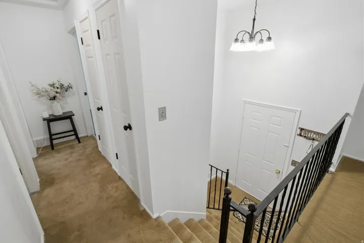 Hallway with carpeted flooring, white paneled doors, and a staircase featuring a black metal railing