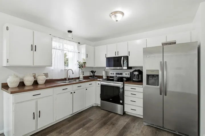 Kitchen featuring wood-finish countertops, white cabinetry, stainless steel appliances, and wood-finish flooring