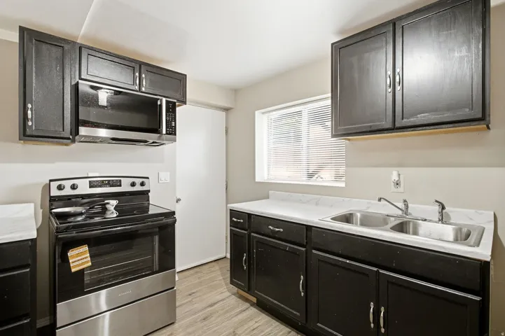 Kitchen featuring dark wood-finish cabinetry, white countertops, stainless steel appliances, and a dual basin sink