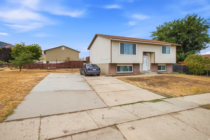 Split-level home featuring light-toned siding, a concrete driveway, and a fenced backyard
