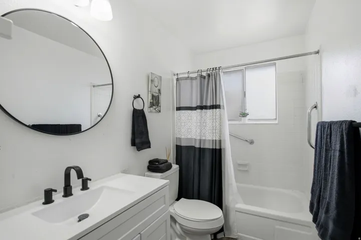 Bathroom featuring a white vanity with integrated sink, matte black faucet, and a circular mirror