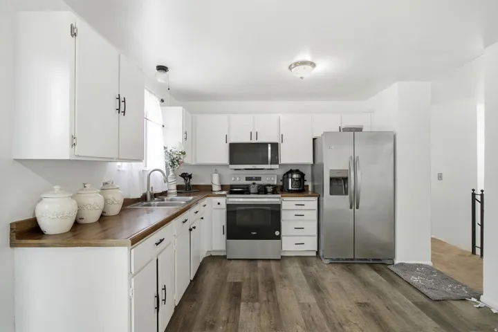 Modern kitchen featuring white cabinetry, wood-finish countertops, stainless steel appliances, a double basin sink, and wood-finish flooring