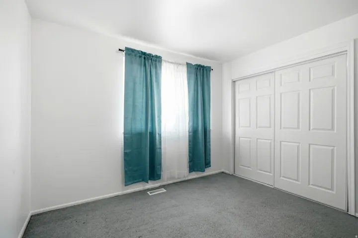 White painted walls, carpeted flooring, and a window with a curtain rod