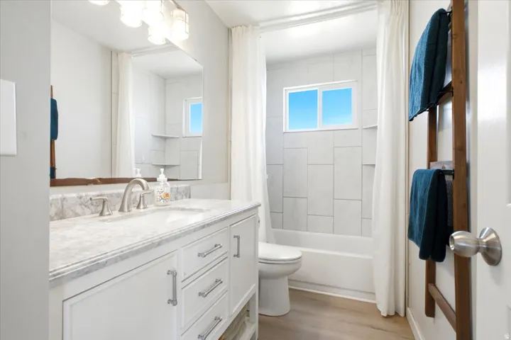 White shaker-style vanity with chrome hardware, a single basin sink, and a stone countertop