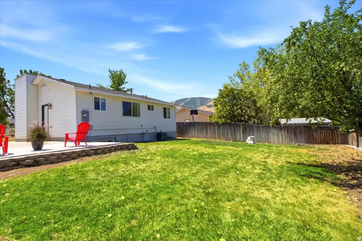 Expansive grassy backyard with a concrete patio, retaining wall, and wood fence