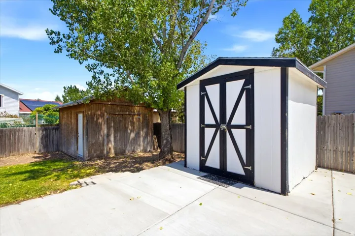 Backyard featuring a new storage shed with barn-style doors, a mature tree, and a concrete pad