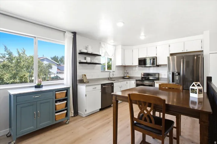 Light wood-finish flooring, white cabinetry, stainless steel appliances, white subway tile backsplash, and a large window