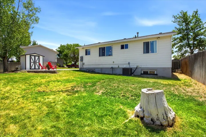 Expansive grassy yard with a white vinyl-sided exterior, a detached storage shed, a stone-edged patio area, and a wood privacy fence