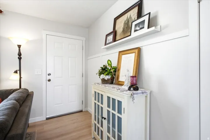 Light-toned wood-finish flooring, white paneled door with brass hardware, and white board and batten wall detailing