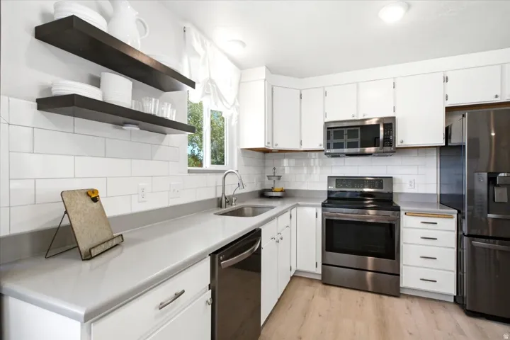 Kitchen featuring white cabinetry, gray countertops, stainless steel appliances, subway tile backsplash, and light wood-finish flooring