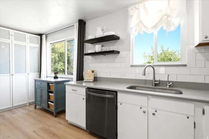 Kitchen featuring wood-finish flooring, white cabinetry with frosted glass panels, subway tile backsplash, and a large window above the sink