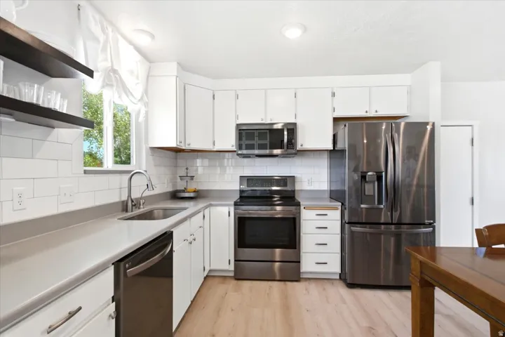 Kitchen featuring white cabinetry, light-toned countertops, subway tile backsplash, stainless steel appliances, and wood-finish flooring