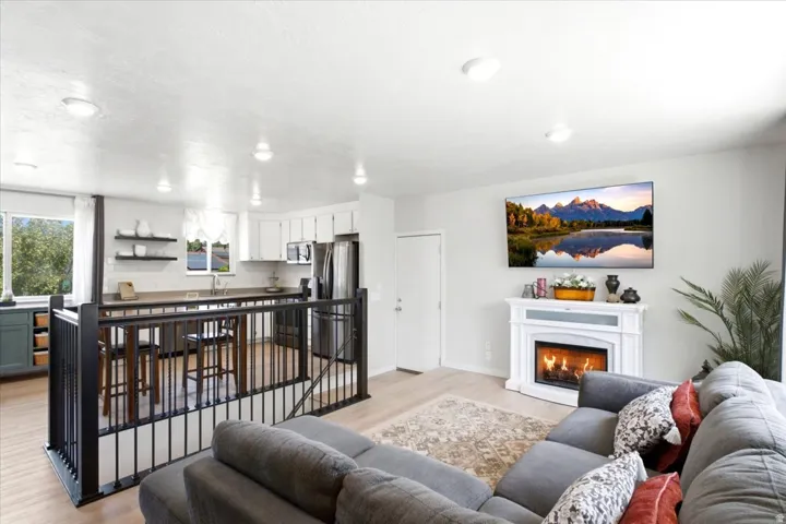 Open-concept living area with fireplace, recessed lighting, wood-finish flooring, and a kitchen featuring white cabinetry and stainless steel appliances