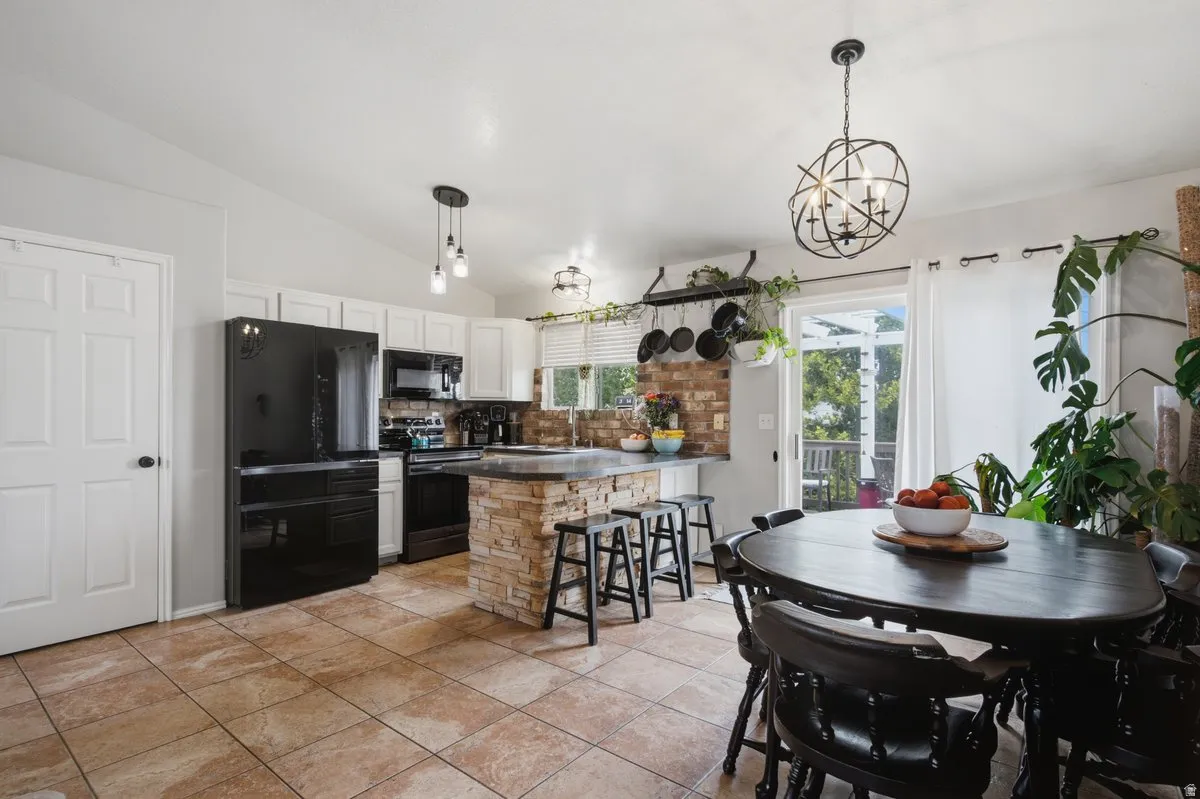 Kitchen featuring white cabinetry, black appliances, a stone-clad island, and tile flooring