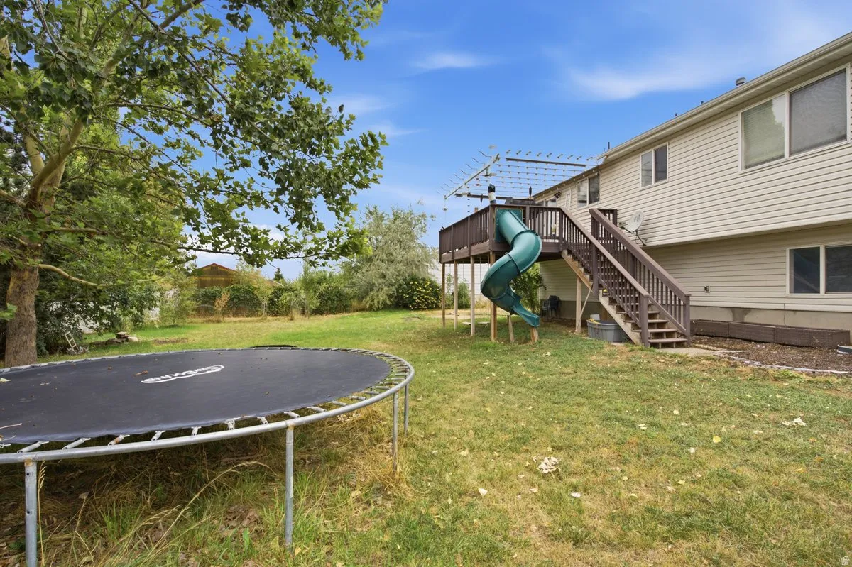 Rear exterior featuring a wood-finish deck with stairs, a vinyl-sided facade, and established trees