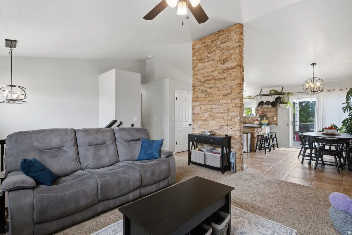 Natural stone-clad accent wall, vaulted ceiling, ceiling fan with light fixture, tile flooring, and sliding glass door