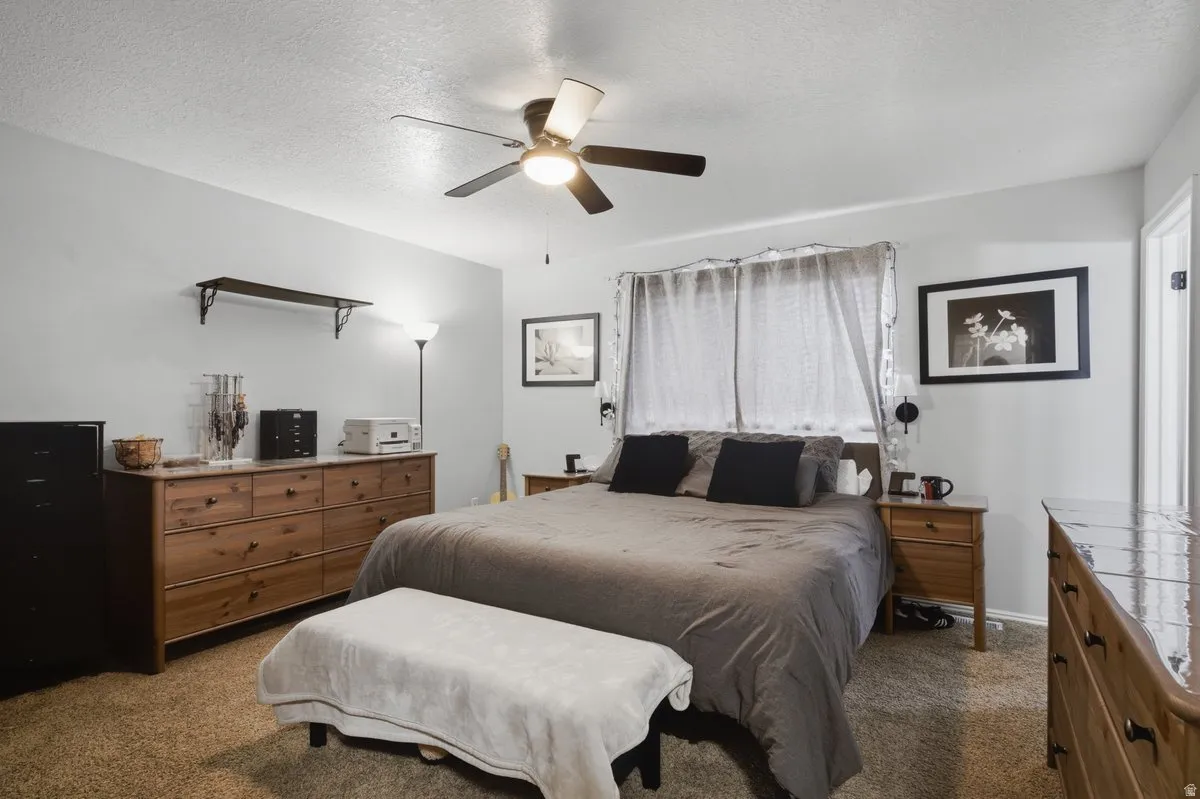 Wall-mounted shelving unit, ceiling fan with integrated lighting, wood-finish dressers, and a window with curtain rods