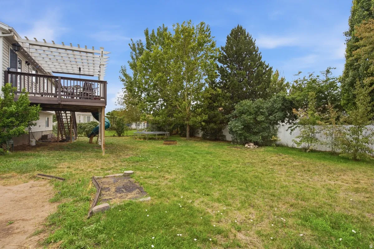 Elevated wood deck with a slatted pergola, expansive grassed yard, mature trees, and a white privacy fence