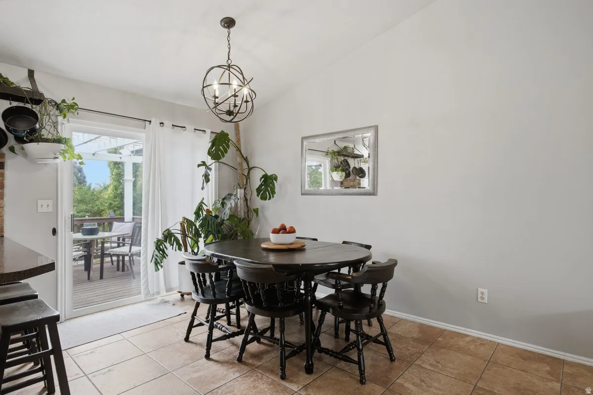 Vaulted ceiling with an orb chandelier, sliding glass door, tiled flooring, and a mirrored wall accent