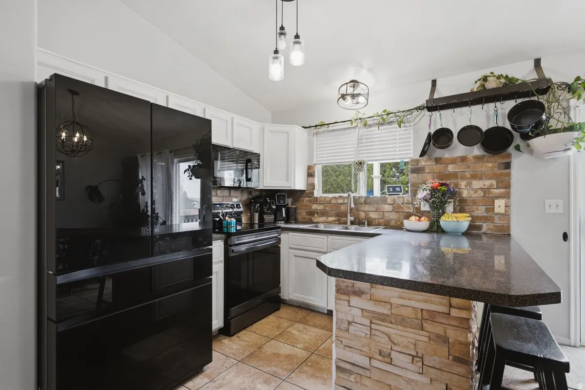 White cabinetry, black appliances, a stone-finish breakfast bar, tiled flooring, and a brick-finish backsplash