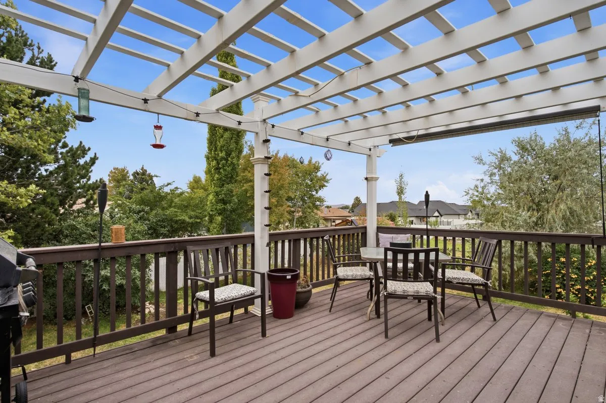 Expansive wooden deck featuring a white pergola structure, dark wood railings, and an integrated overhead heating element