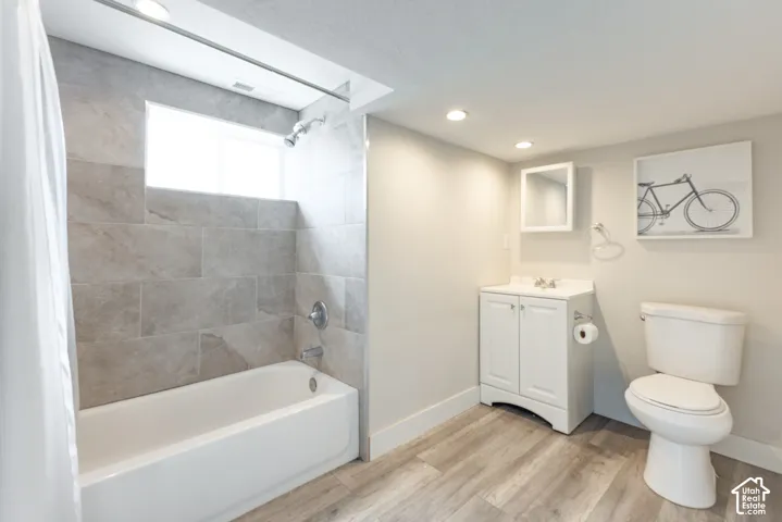 Wood-finish flooring, tiled bath/shower, white vanity, and toilet