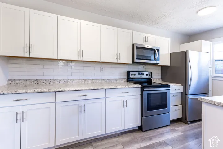 White shaker-style cabinetry, stainless steel appliances, speckled stone-finish countertops, subway tile backsplash, and wood-finish flooring