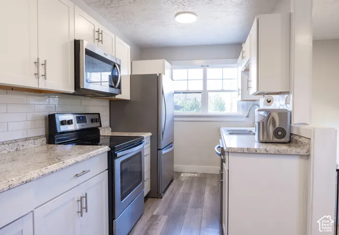 Kitchen featuring white cabinetry, stone-finish countertops, stainless steel appliances, a subway tile backsplash, and wood-finish flooring