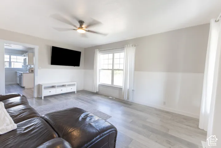 Wood-finish flooring, half-wall wainscoting, a ceiling fan with integrated lighting, and a large window