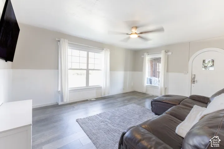 Wood-finish flooring, half-wall paneling, ceiling fan, transom window, and a white arched entry door