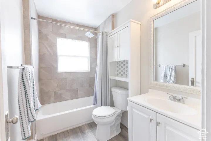 Bathroom featuring a white vanity with integrated sink, a framed mirror, an overhead light fixture, wood-finish flooring, and a tiled shower with a window