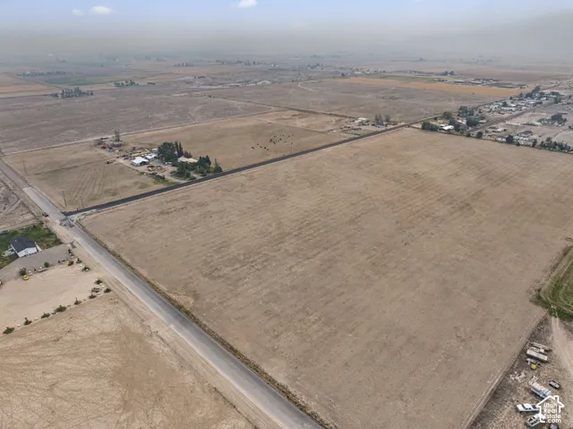 Expansive agricultural property featuring a vast, open field, bordered by paved and unpaved roads