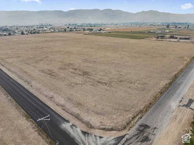 Expansive land parcel featuring clear ground, paved road access, and distant mountain scenery