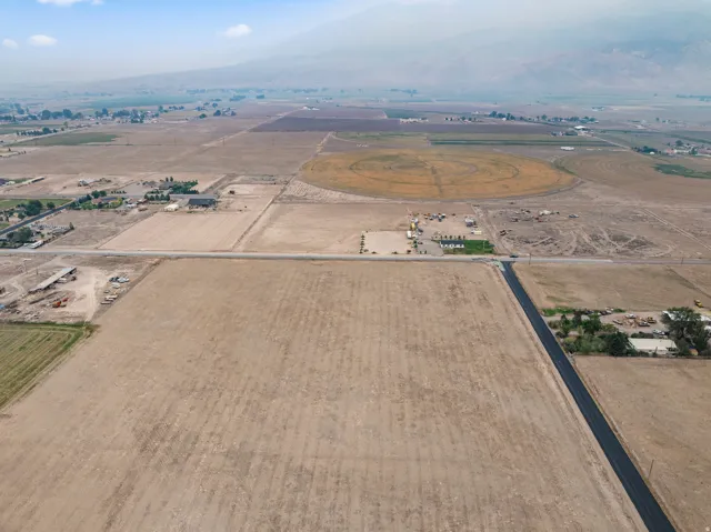 Expansive rural property with agricultural fields, paved road access, and distant mountain backdrop
