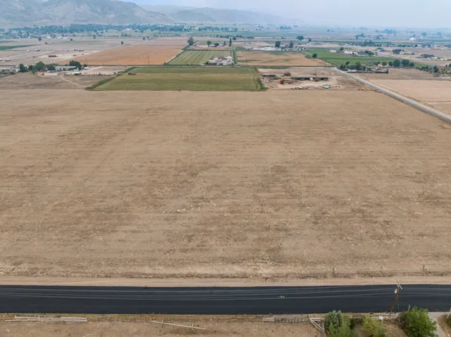 Expansive arid lot with distant mountain backdrop, featuring an asphalt road and surrounding agricultural fields