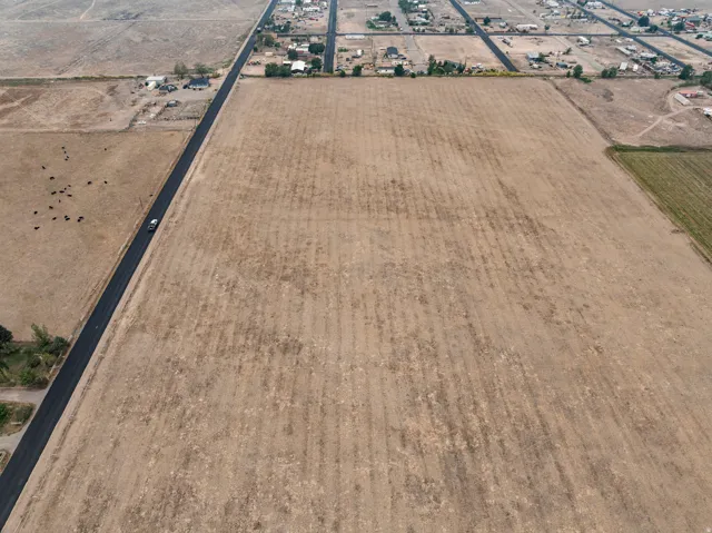 Expansive agricultural land featuring a paved road, scattered structures, and adjacent cultivated fields