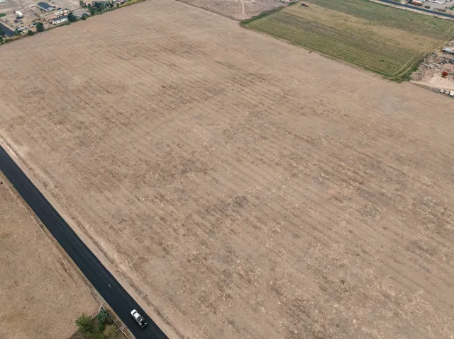 Expansive open land area with visible tilled earth and bordering paved road