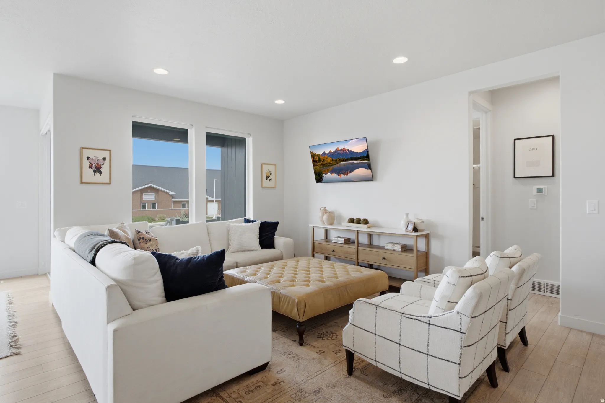 Bright, open-concept living area featuring recessed ceiling lighting, large windows with black-framed glazing, and light wood-finish flooring throughout