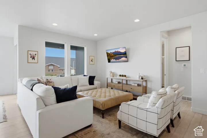 Bright, open-concept living area featuring recessed ceiling lighting, large windows with black-framed glazing, and light wood-finish flooring throughout