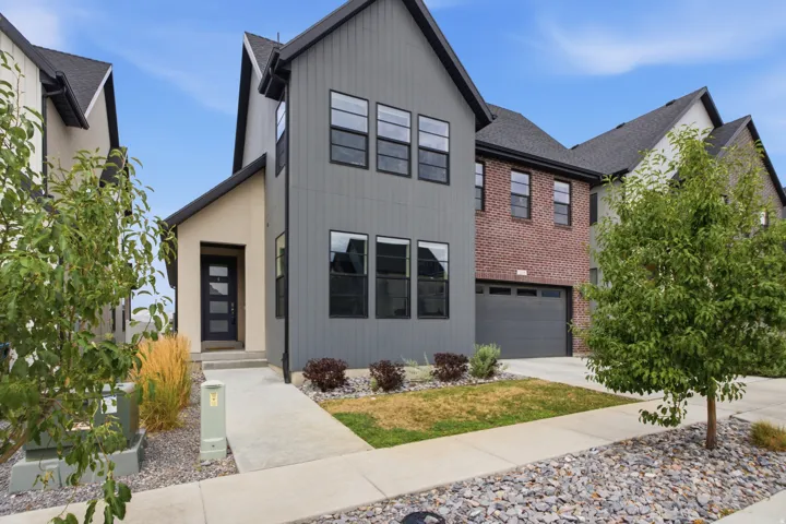 Contemporary exterior featuring gray vertical siding, dark framed windows, a covered entry, and an integrated garage