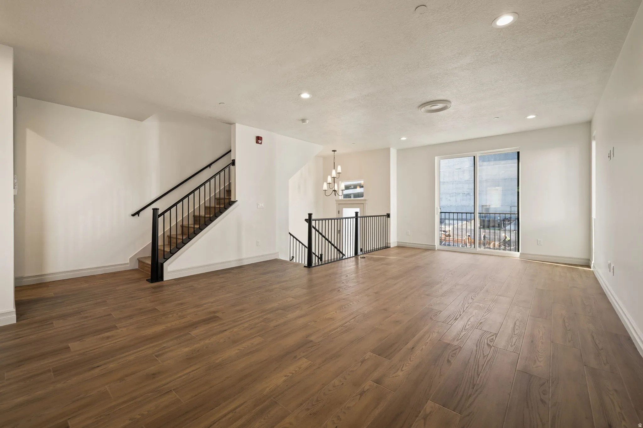 Expansive living area with wood-finish flooring, recessed lighting, and a sliding glass door leading to a balcony