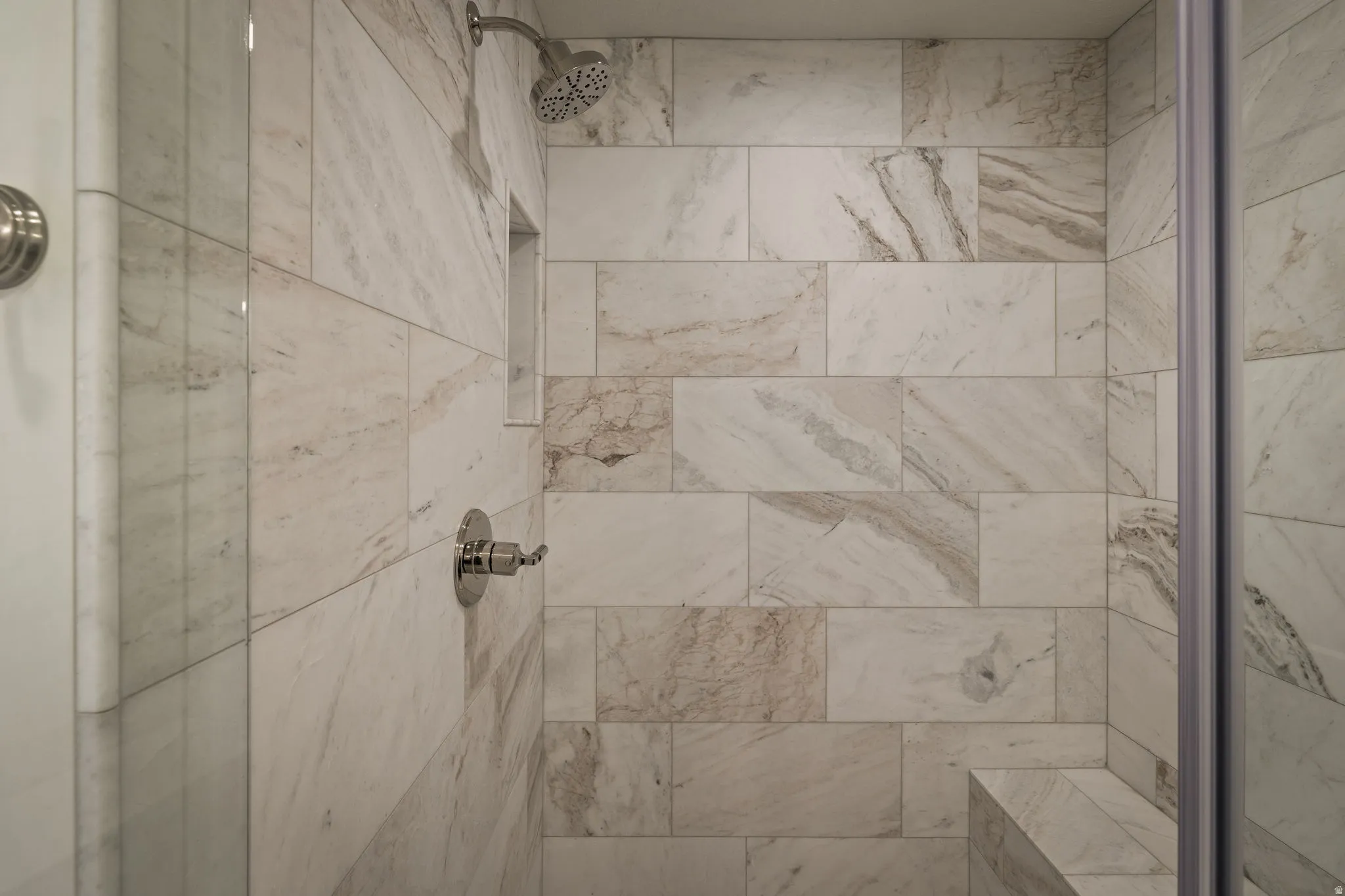 Tiled shower stall featuring a built-in niche, integrated bench, and brushed nickel fixtures