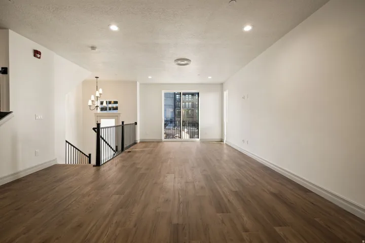 Spacious living area featuring wood-finish flooring, white walls, recessed lighting, and a sliding glass door