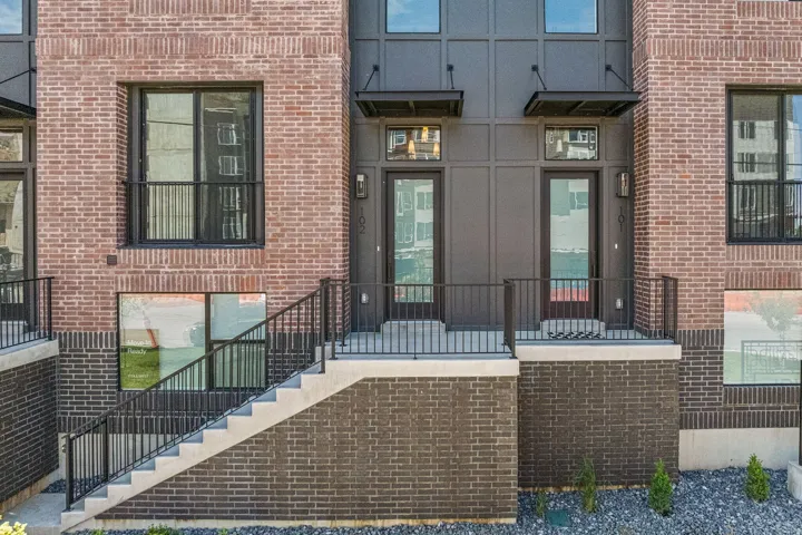 Brick facade with contrasting dark brick lower level, concrete stairs, and black metal railings