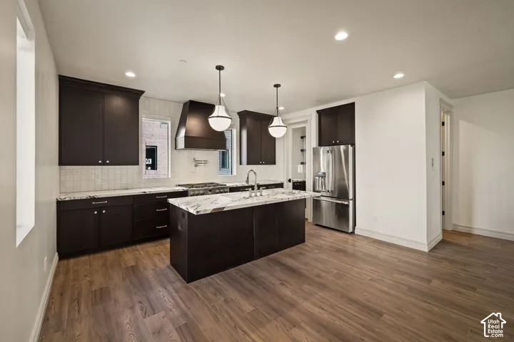 Gourmet kitchen featuring dark wood cabinetry, white tile backsplash, a center island with a light-toned countertop, and wood-finish flooring