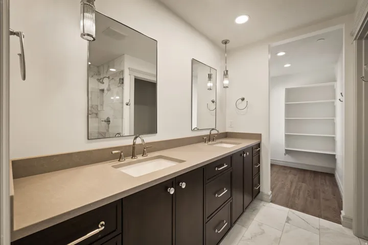 Dual vanity with integrated sinks, stone-finish countertop, dark wood-finish cabinetry, and contemporary pendant lighting