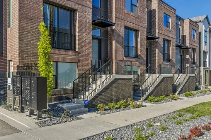 Brick exterior with black accents, concrete entry stairs with black railings, ground-level windows, and an established sidewalk