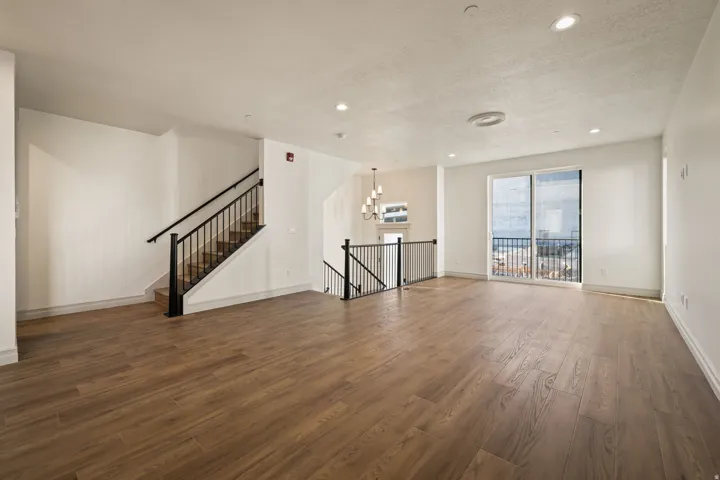 Expansive living area with wood-finish flooring, recessed lighting, and a sliding glass door leading to a balcony