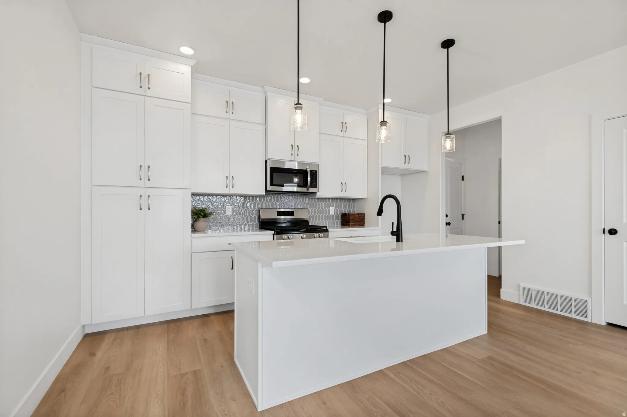 White cabinetry, wood-finish flooring, white kitchen island with counter, stainless steel appliances, and pendant lighting